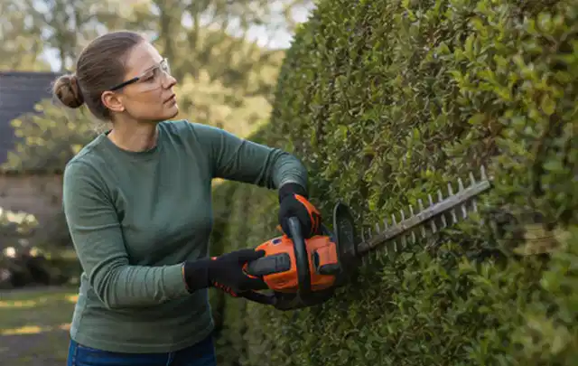 Person schneidet eine dichte Gartenhecke mit Schutzbrille und sicherem Stand; Thema Akku Gartengeräte, Schwerpunkt Bestenliste; Ergebnis.