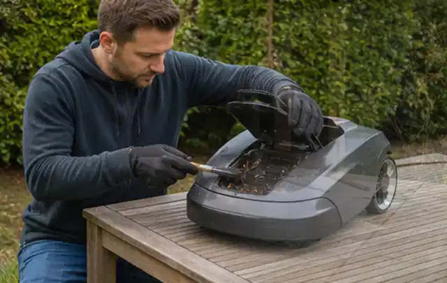 Person wartet einen geöffneten Mähroboter auf einem stabilen Gartentisch; Thema Akku Gartengeräte, Schwerpunkt Gärten mit kleiner Fläche; Ergebnis.