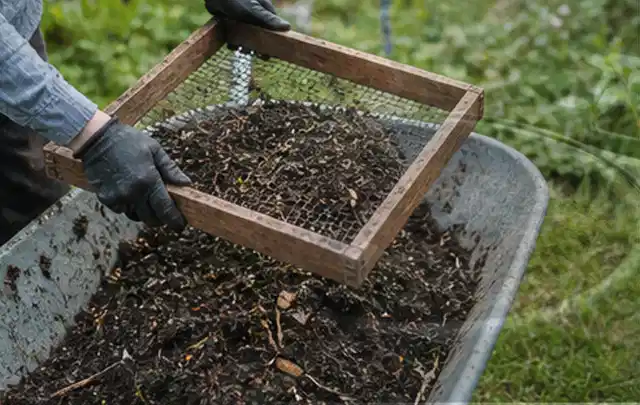 Behandschuhte Hände sieben reifen Kompost über einer Gartenschubkarre; Thema Anleitungen, Schwerpunkt Ratgeber; Ausgangslage.
