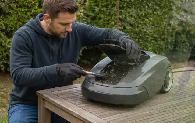 Person wartet einen geöffneten Mähroboter auf einem stabilen Gartentisch; Thema Astscheren, Schwerpunkt Sicherheit; Kontrolle.