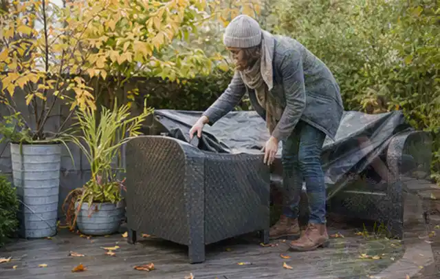 Person deckt Gartenmöbel vor der kalten Jahreszeit sorgfältig ab; Thema Aufstellpools, Schwerpunkt Ersatzteile; Praxisalltag.