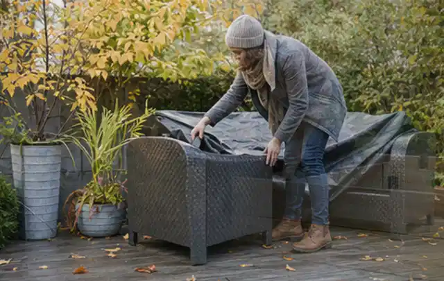 Person deckt Gartenmöbel vor der kalten Jahreszeit sorgfältig ab; Thema Aufstellpools, Schwerpunkt Fehlerhilfe; Praxisalltag.