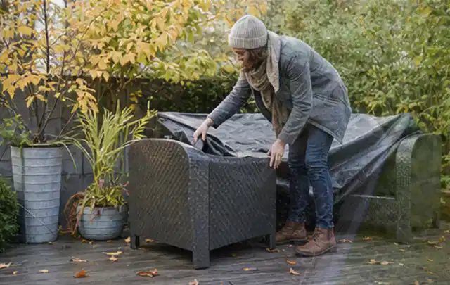 Person deckt Gartenmöbel vor der kalten Jahreszeit sorgfältig ab; Thema Aufstellpools, Schwerpunkt Winterlager; Ausgangslage.