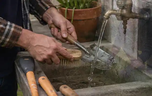Hände reinigen gebrauchte Gartengeräte mit Bürste und Wasser am Außenbecken; Thema Bosch Indego, Schwerpunkt Bestenliste; Umsetzung.