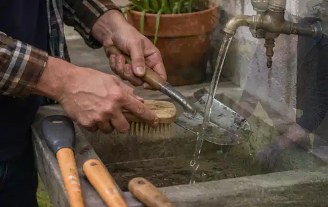 Hände reinigen gebrauchte Gartengeräte mit Bürste und Wasser am Außenbecken; Thema Bosch Indego, Schwerpunkt Checkliste; Praxisalltag.
