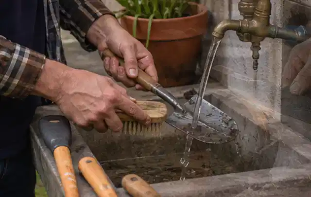 Hände reinigen gebrauchte Gartengeräte mit Bürste und Wasser am Außenbecken; Thema Bosch Indego, Schwerpunkt Fehlerhilfe; Kontrolle.