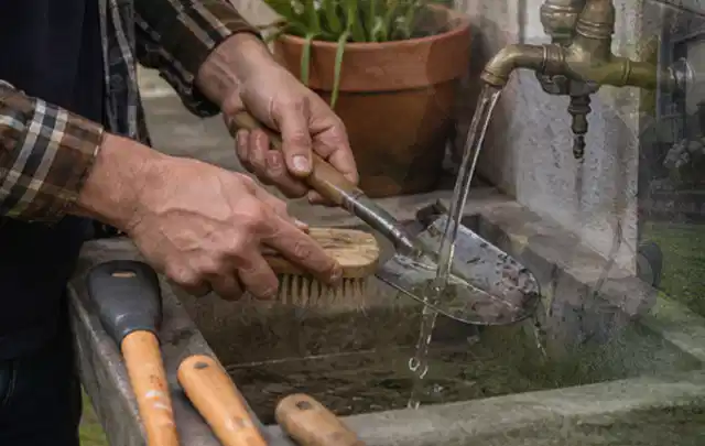 Hände reinigen gebrauchte Gartengeräte mit Bürste und Wasser am Außenbecken; Thema Bosch Indego, Schwerpunkt Gärten mit kleiner Fläche; Ausgangslage.