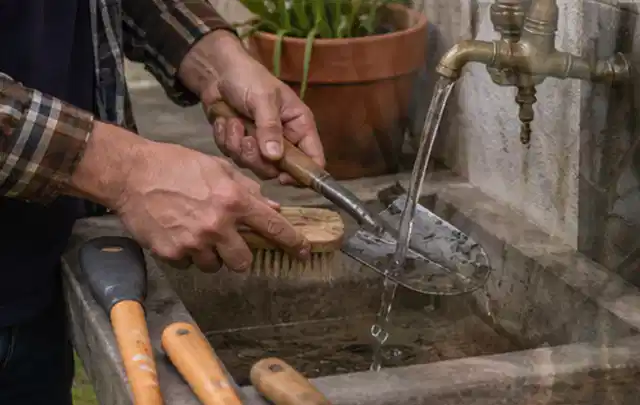 Hände reinigen gebrauchte Gartengeräte mit Bürste und Wasser am Außenbecken; Thema Bosch Indego, Schwerpunkt Kosten; Kontrolle.