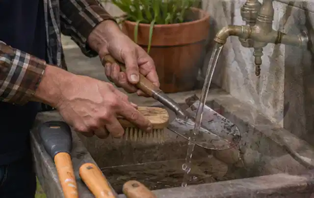 Hände reinigen gebrauchte Gartengeräte mit Bürste und Wasser am Außenbecken; Thema Bosch Indego, Schwerpunkt Mähroboter; Umsetzung.