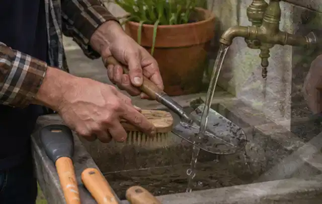 Hände reinigen gebrauchte Gartengeräte mit Bürste und Wasser am Außenbecken; Thema Bosch Indego, Schwerpunkt Reparatur; Ausgangslage.