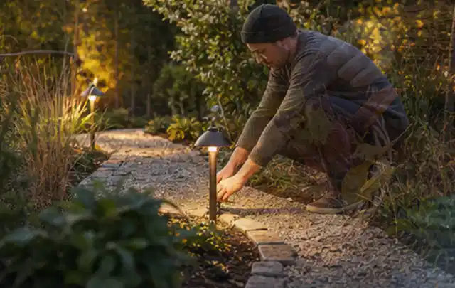Person richtet eine niedrige warm leuchtende Gartenlampe am Kiesweg aus; Thema Cookie Einstellungen, Schwerpunkt Privatsphäre Einstellungen; Umsetzung.