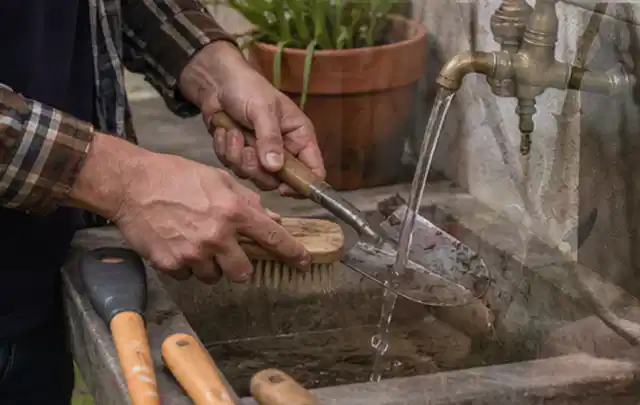 Hände reinigen gebrauchte Gartengeräte mit Bürste und Wasser am Außenbecken; Thema Dreame A1, Schwerpunkt Fehlerhilfe; Ergebnis.