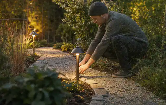Person richtet eine niedrige warm leuchtende Gartenlampe am Kiesweg aus; Thema Dreame A1, Schwerpunkt Fehlerhilfe; Praxisalltag.