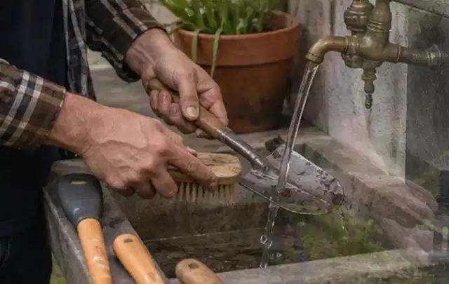 Hände reinigen gebrauchte Gartengeräte mit Bürste und Wasser am Außenbecken; Thema Dreame A1, Schwerpunkt Gärten mit großer Fläche; Umsetzung.