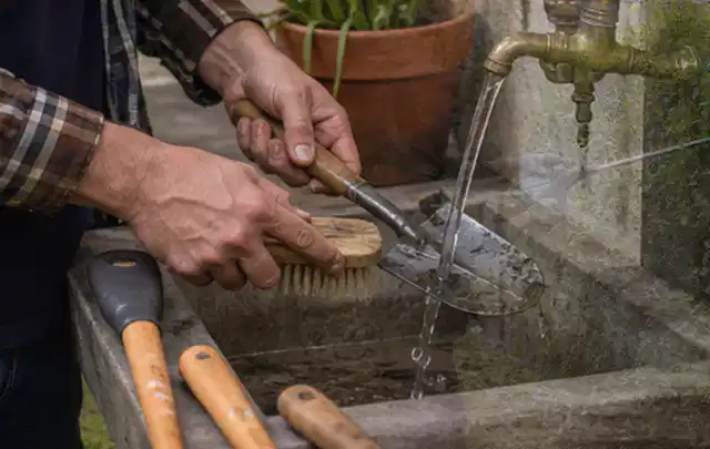 Hände reinigen gebrauchte Gartengeräte mit Bürste und Wasser am Außenbecken; Thema Dreame A1, Schwerpunkt Nachhaltigkeit; Umsetzung.