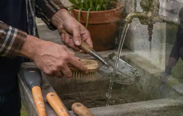 Hände reinigen gebrauchte Gartengeräte mit Bürste und Wasser am Außenbecken; Thema Dreame A1, Schwerpunkt Sicherheit; Kontrolle.