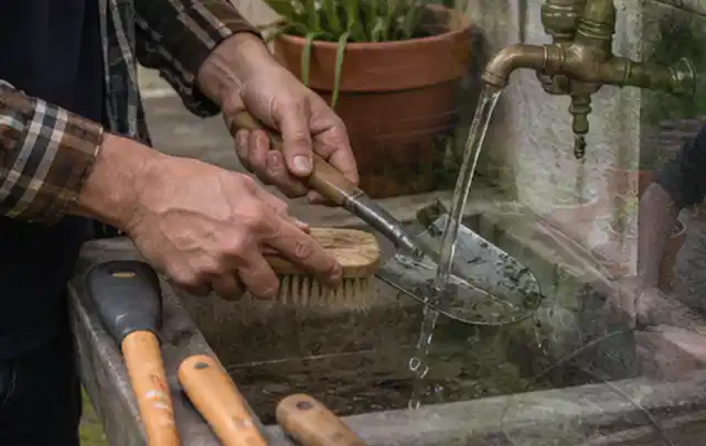 Hände reinigen gebrauchte Gartengeräte mit Bürste und Wasser am Außenbecken; Thema Ecovacs Goat, Schwerpunkt Anwendung; Ausgangslage.