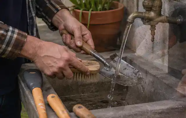 Hände reinigen gebrauchte Gartengeräte mit Bürste und Wasser am Außenbecken; Thema Ecovacs Goat, Schwerpunkt Kaufberatung; Umsetzung.