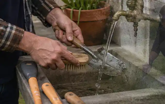 Hände reinigen gebrauchte Gartengeräte mit Bürste und Wasser am Außenbecken; Thema Ecovacs Goat, Schwerpunkt Winterlager; Ausgangslage.