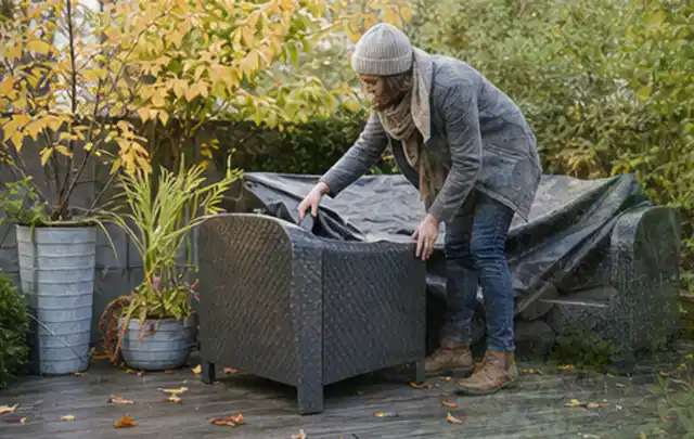 Person deckt Gartenmöbel vor der kalten Jahreszeit sorgfältig ab; Thema Einbaupools, Schwerpunkt Dimensionierung; Kontrolle.