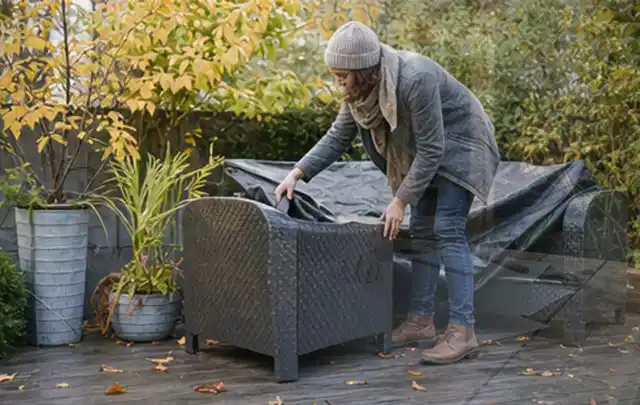 Person deckt Gartenmöbel vor der kalten Jahreszeit sorgfältig ab; Thema Einbaupools, Schwerpunkt Systemvergleich; Praxisalltag.