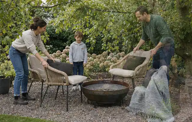 Familie stellt wetterfeste Sessel an einem geschützten Sitzplatz im Garten auf; Thema Einbaupools, Schwerpunkt Winterlager; Praxisalltag.