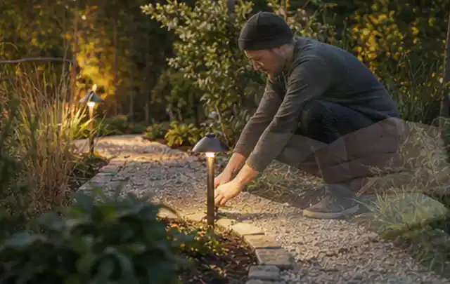 Person richtet eine niedrige warm leuchtende Gartenlampe am Kiesweg aus; Thema Feuerschalen, Schwerpunkt Kaufberatung; Ergebnis.