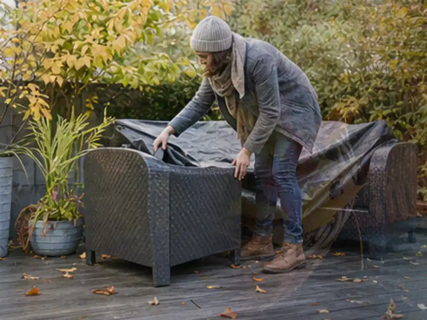 Person deckt Gartenmöbel vor der kalten Jahreszeit sorgfältig ab; Thema Feuerschalen, Schwerpunkt Vergleich; Titelbild.