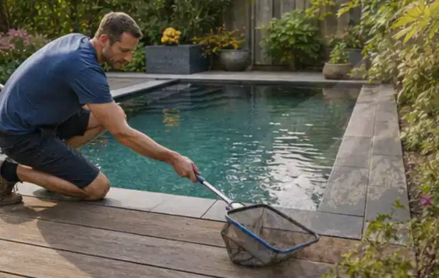 Person entfernt Blätter mit einem Kescher aus einem kleinen Gartenpool; Thema Feuerschalen, Schwerpunkt Winterlager; Praxisalltag.