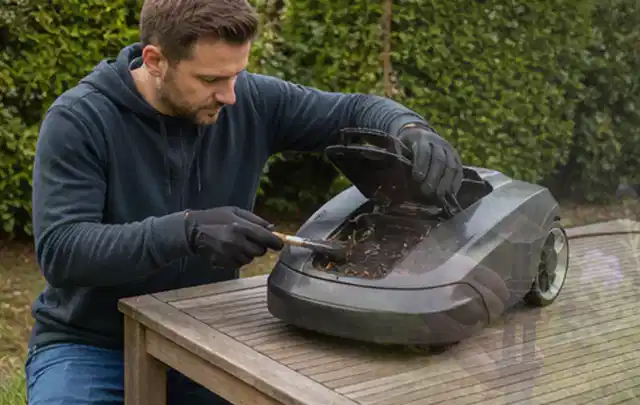 Person wartet einen geöffneten Mähroboter auf einem stabilen Gartentisch; Thema Freischneider, Schwerpunkt Reparatur; Umsetzung.
