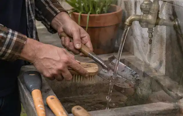 Hände reinigen gebrauchte Gartengeräte mit Bürste und Wasser am Außenbecken; Thema Gardena Sileno, Schwerpunkt Anwendung; Umsetzung.