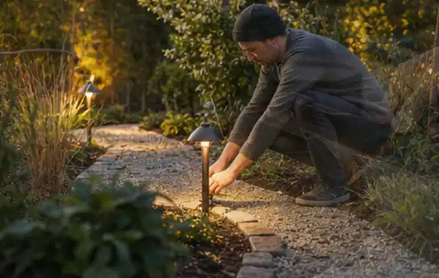 Person richtet eine niedrige warm leuchtende Gartenlampe am Kiesweg aus; Thema Gardena Sileno, Schwerpunkt Fehlerhilfe; Ergebnis.