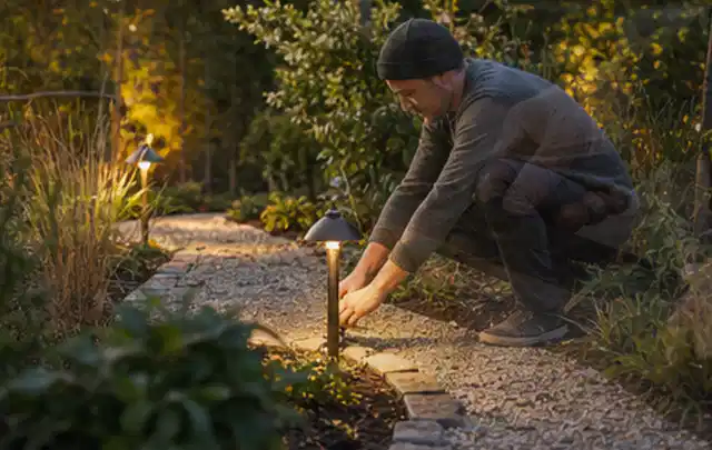 Person richtet eine niedrige warm leuchtende Gartenlampe am Kiesweg aus; Thema Gardena Sileno, Schwerpunkt Kaufberatung; Kontrolle.