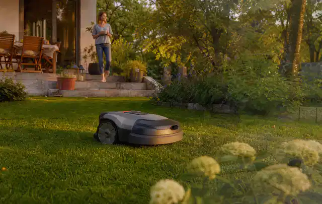 Mähroboter fährt am Abend über einen Rasen im Familiengarten; Thema Gardena Sileno, Schwerpunkt Kosten; Kontrolle.