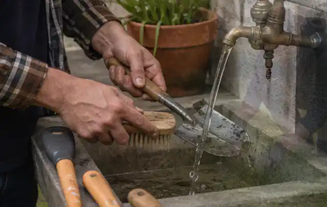 Hände reinigen gebrauchte Gartengeräte mit Bürste und Wasser am Außenbecken; Thema Gardena Sileno, Schwerpunkt Nachhaltigkeit; Ergebnis.