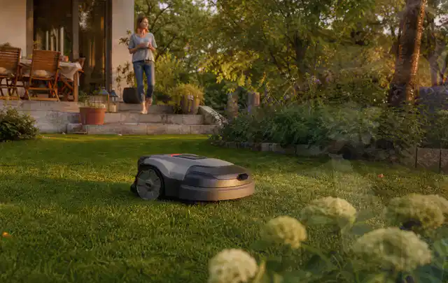 Mähroboter fährt am Abend über einen Rasen im Familiengarten; Thema Gardena Sileno, Schwerpunkt Reinigung; Umsetzung.