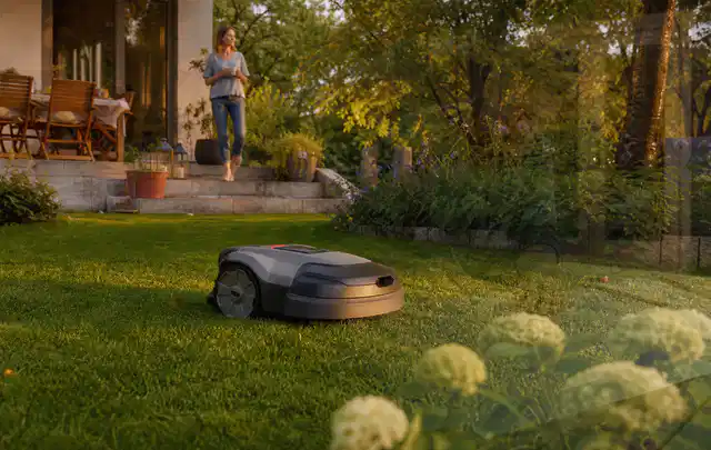 Mähroboter fährt am Abend über einen Rasen im Familiengarten; Thema Gardena Sileno, Schwerpunkt Reparatur; Umsetzung.