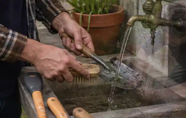 Hände reinigen gebrauchte Gartengeräte mit Bürste und Wasser am Außenbecken; Thema Gardena Sileno, Schwerpunkt Reparatur; Praxisalltag.