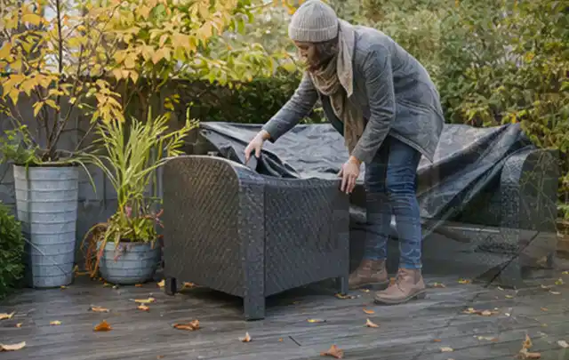 Person deckt Gartenmöbel vor der kalten Jahreszeit sorgfältig ab; Thema Gartenbeleuchtung, Schwerpunkt Anwendung; Ausgangslage.