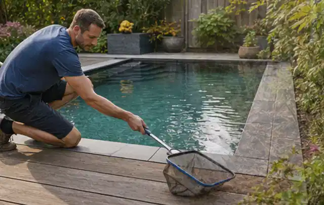 Person entfernt Blätter mit einem Kescher aus einem kleinen Gartenpool; Thema Gartenbeleuchtung, Schwerpunkt Checkliste; Praxisalltag.