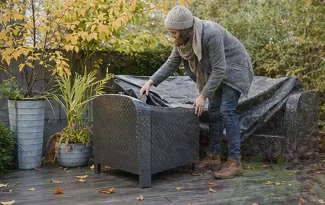 Person deckt Gartenmöbel vor der kalten Jahreszeit sorgfältig ab; Thema Gartenbeleuchtung, Schwerpunkt Leistung; Umsetzung.