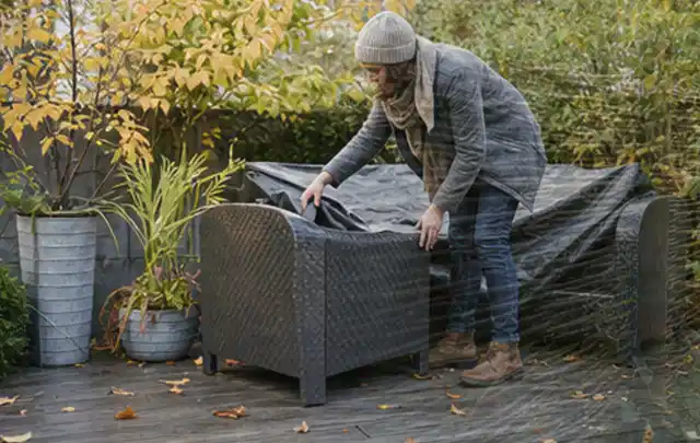 Person deckt Gartenmöbel vor der kalten Jahreszeit sorgfältig ab; Thema Gartenbeleuchtung, Schwerpunkt Outdoor Freizeit; Kontrolle.