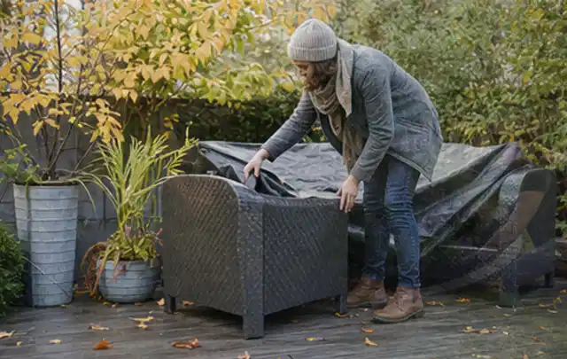 Person deckt Gartenmöbel vor der kalten Jahreszeit sorgfältig ab; Thema Gartenbeleuchtung, Schwerpunkt Testkriterien; Umsetzung.