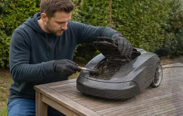 Person wartet einen geöffneten Mähroboter auf einem stabilen Gartentisch; Thema Gartengeräte, Schwerpunkt Themenwelt; Ergebnis.