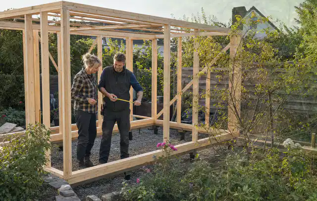 Person plant den Bau eines Gartenhauses auf einer vorbereiteten Fläche; Thema Gartenhaus aus Metall, Schwerpunkt Materialwahl; Umsetzung.