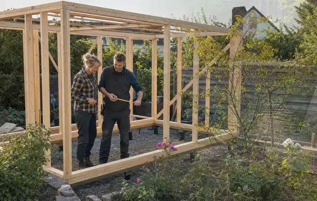 Person plant den Bau eines Gartenhauses auf einer vorbereiteten Fläche; Thema Gartenhaus aus Metall, Schwerpunkt Pflege; Praxisalltag.