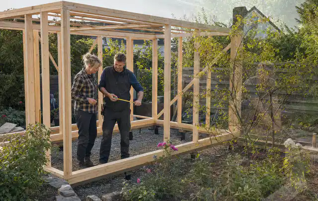 Person plant den Bau eines Gartenhauses auf einer vorbereiteten Fläche; Thema Gartenhaus Dach, Schwerpunkt Pflege; Praxisalltag.