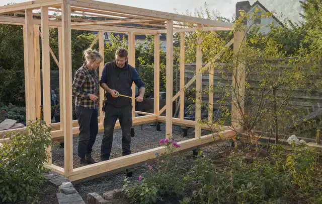 Person plant den Bau eines Gartenhauses auf einer vorbereiteten Fläche; Thema Gartenhaus Fenster, Schwerpunkt Kosten; Kontrolle.