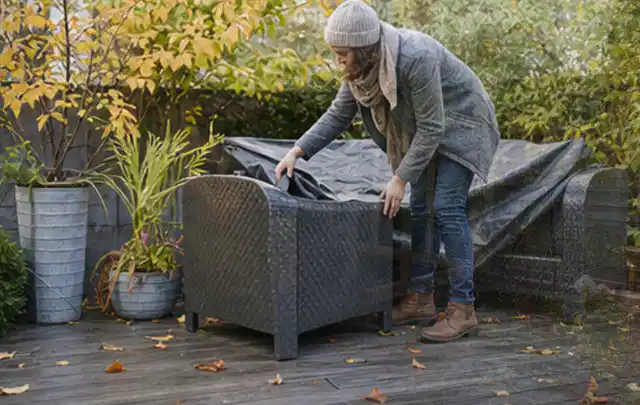 Person deckt Gartenmöbel vor der kalten Jahreszeit sorgfältig ab; Thema Gartenlounges, Schwerpunkt Anwendung; Kontrolle.