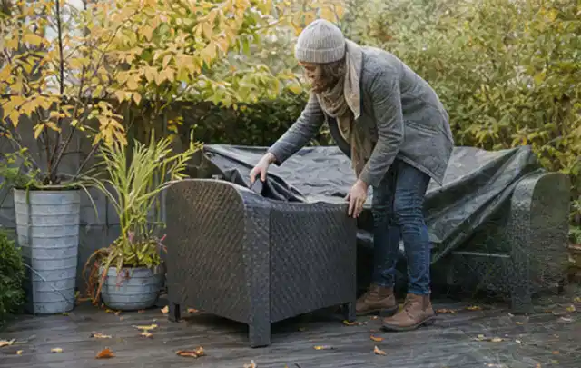 Person deckt Gartenmöbel vor der kalten Jahreszeit sorgfältig ab; Thema Gartenlounges, Schwerpunkt Bestenliste; Ausgangslage.
